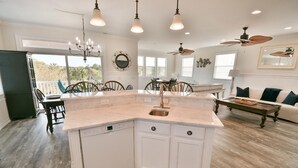 A spacious kitchen with a central island, dining area with chairs, and a living room with a sofa.