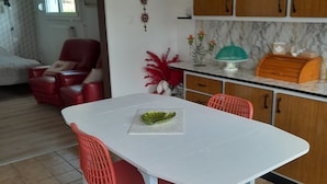 A dining area with a white table, red chairs, a green decorative plate, and a kitchen in the background.