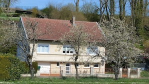 A two-story house with a red-tiled roof, a small front porch, and a garden area with a pond.