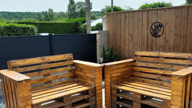 Two wooden benches made of pallets, placed on a tiled patio with a wooden fence and greenery in the background.