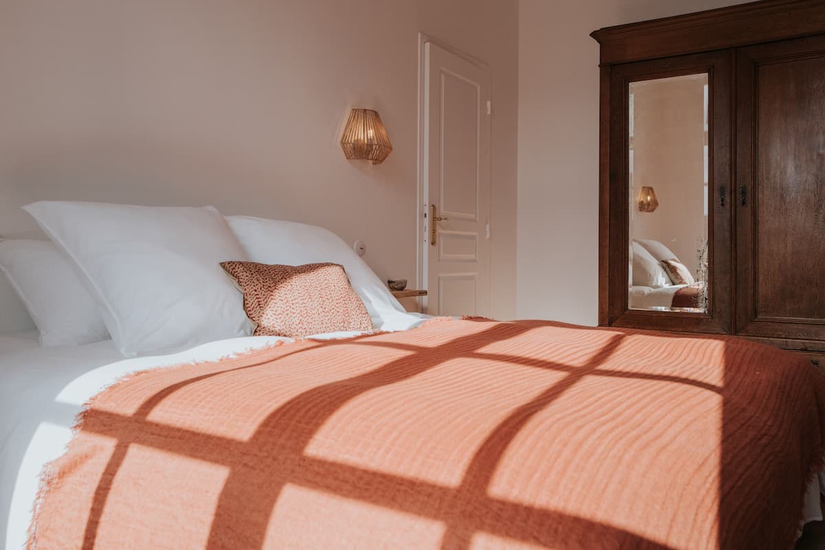Un dormitorio con cama, almohadas, un armario de madera y una lámpara de pared.