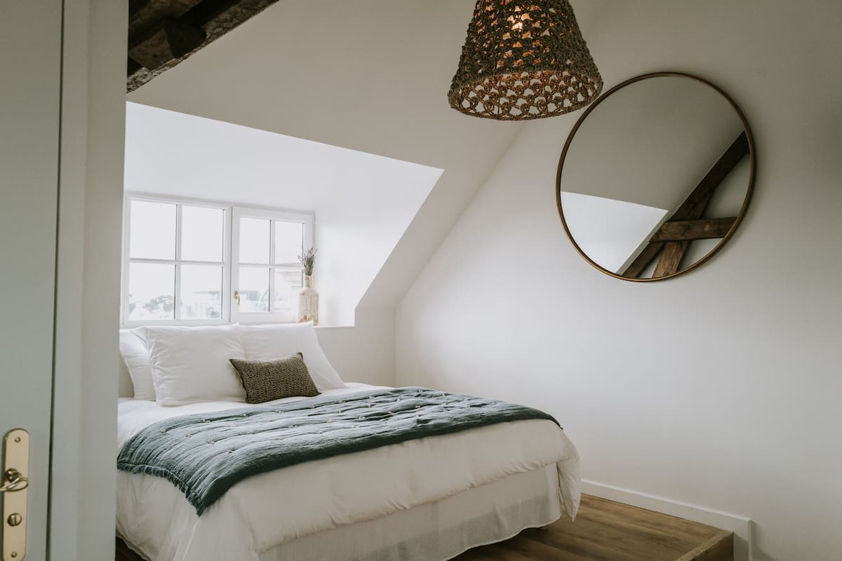 Un dormitorio con una cama grande, una ventana, una lámpara en el techo y un espejo redondo.