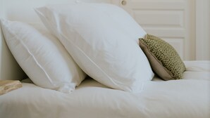 A bedroom with a bed, white pillows, a textured throw pillow, and a wall-mounted light fixture. - La Brise (Roscoff)