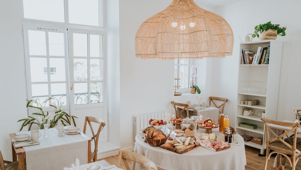 A dining area with a white table set for breakfast, featuring bread, fruits, and beverages. - La Brise (Roscoff)