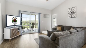 Een moderne woonkamer met een grijze bank, een flatscreen televisie en een plafondventilator.