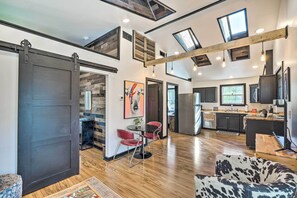 Een ruime woonkamer met een grote schuifdeur, een eettafel met rode stoelen, een bank met een koeienhuidprint, en een keuken met een groot schiereiland en moderne apparatuur.