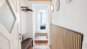 A hallway with a tiled floor, wooden beams, a bench, a radiator, and a wall-mounted clock. - 🌾 **Willkommen im „Huus an`t Koornfeld“ – Ihre Auszeit im Grünen** (Osteel)