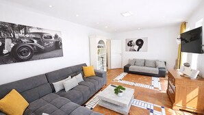 A modern living room with a grey sectional sofa, a smaller grey sofa, a coffee table with a plant, and a flat-screen TV. - 🌾 **Willkommen im „Huus an`t Koornfeld“ – Ihre Auszeit im Grünen** (Osteel)