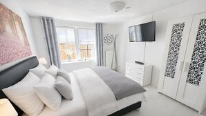 A modern bedroom with a bed, bedside table, TV, wardrobe, and a window with curtains. - 🌾 **Willkommen im „Huus an`t Koornfeld“ – Ihre Auszeit im Grünen** (Osteel)