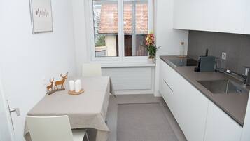Eine kompakte Küche mit Essbereich, ausgestattet mit einem Fenster, weißen Schränken, einer Spüle und einem kleinen Tisch mit einer dekorativen Mittelstück.