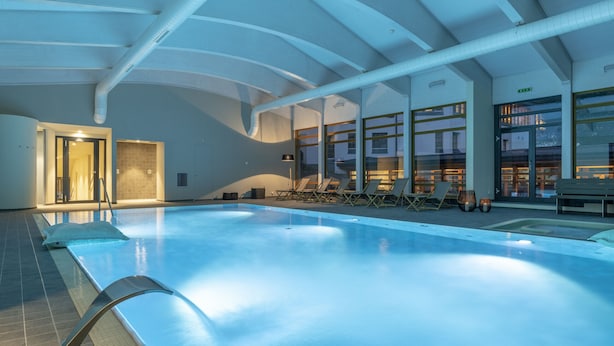 Ein Innenpool mit klaren Glaswänden, Liegestühlen und modernem architektonischem Design.