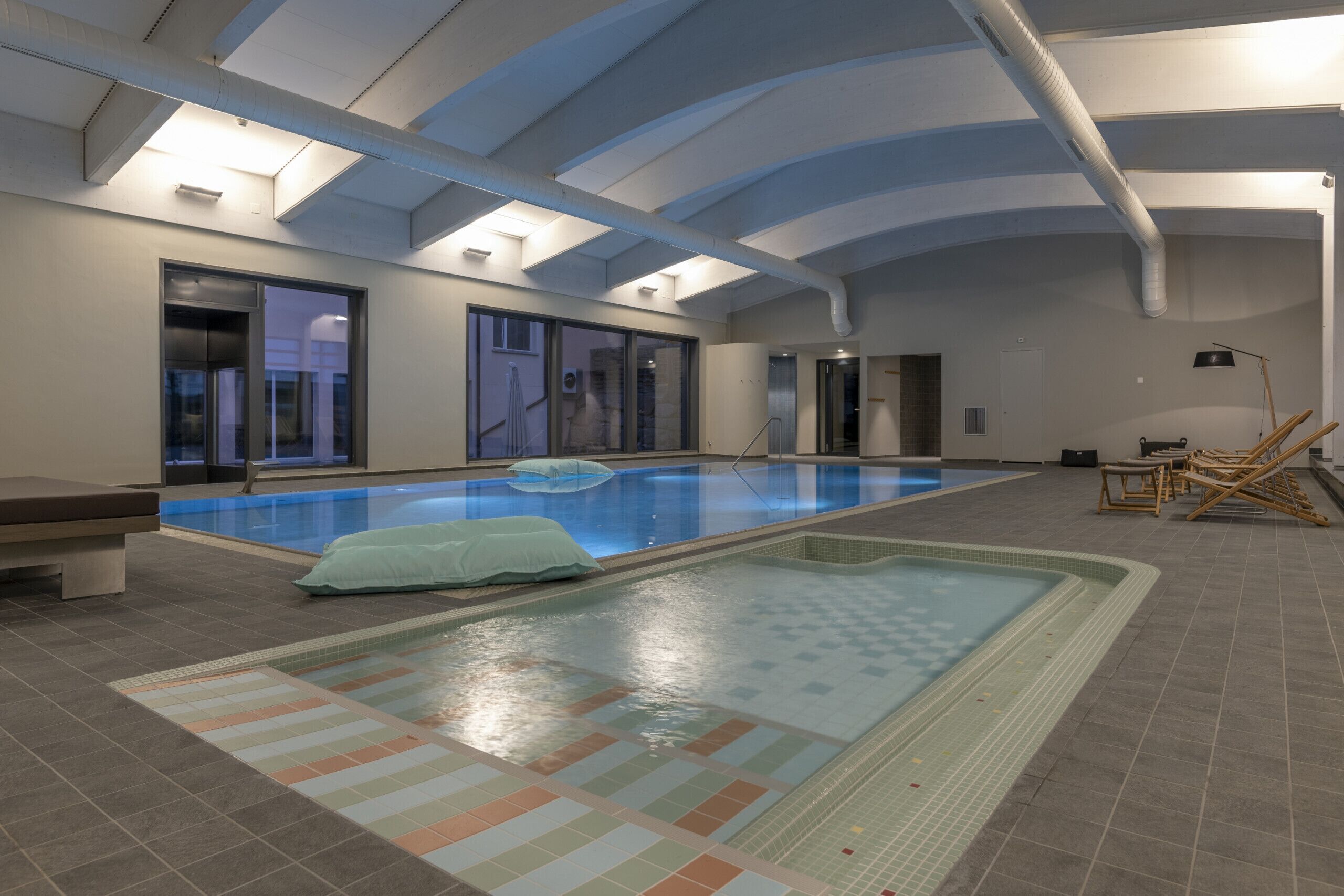 Una piscina interior con agua cristalina, suelo de baldosas y un banco.