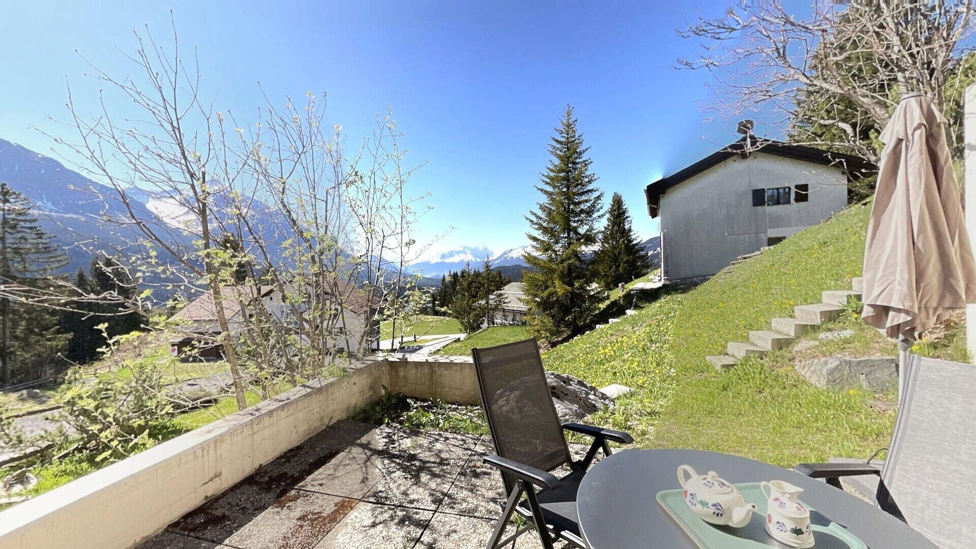 Une terrasse avec une table et des chaises, un petit bâtiment et un paysage montagneux en arrière-plan.