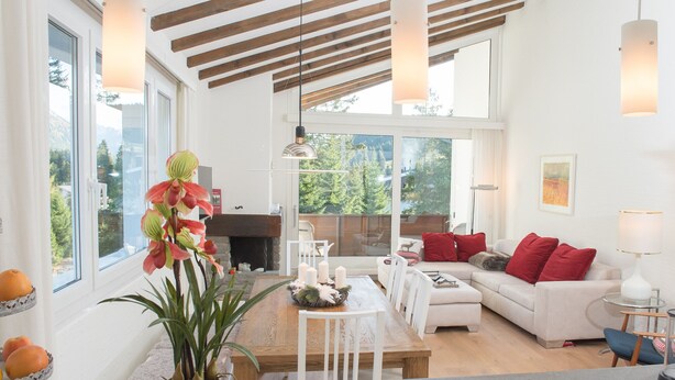 A spacious living area with a fireplace, a dining table, and a sofa with red cushions. - Attic apartment with pool, sauna, and fireplace (Lenzerheide/Lai)