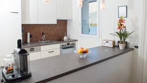 A modern kitchen with white cabinets, a large window, a fruit bowl, and a coffee maker. - Attic apartment with pool, sauna, and fireplace (Lenzerheide/Lai)