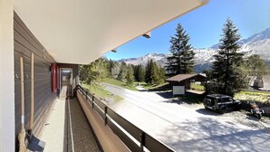 Un balcon donnant sur une route de montagne, une voiture garée et un petit bâtiment.
