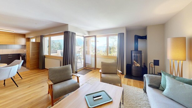 Une chambre d’hôtel moderne avec un plancher en bois, un coin repas comprenant une table et des chaises, un canapé, une télévision, une cheminée et de grandes fenêtres donnant sur l’extérieur.