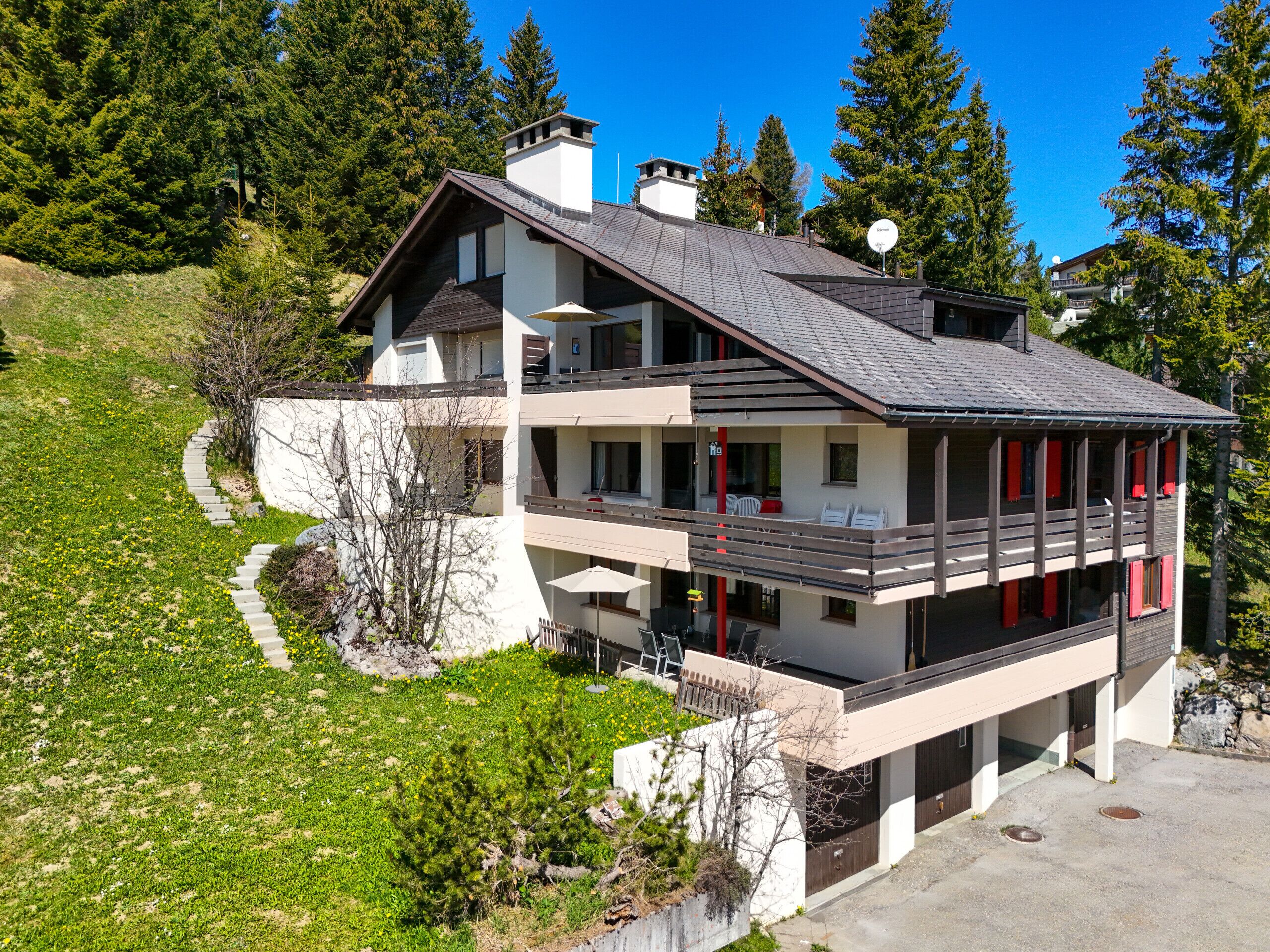 Une maison moderne à deux étages, dotée d’un balcon et entourée de verdure et d’arbres.