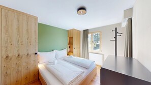 Ein Schlafzimmer mit Bett, Holzschrank und einem Fenster mit Vorhängen.