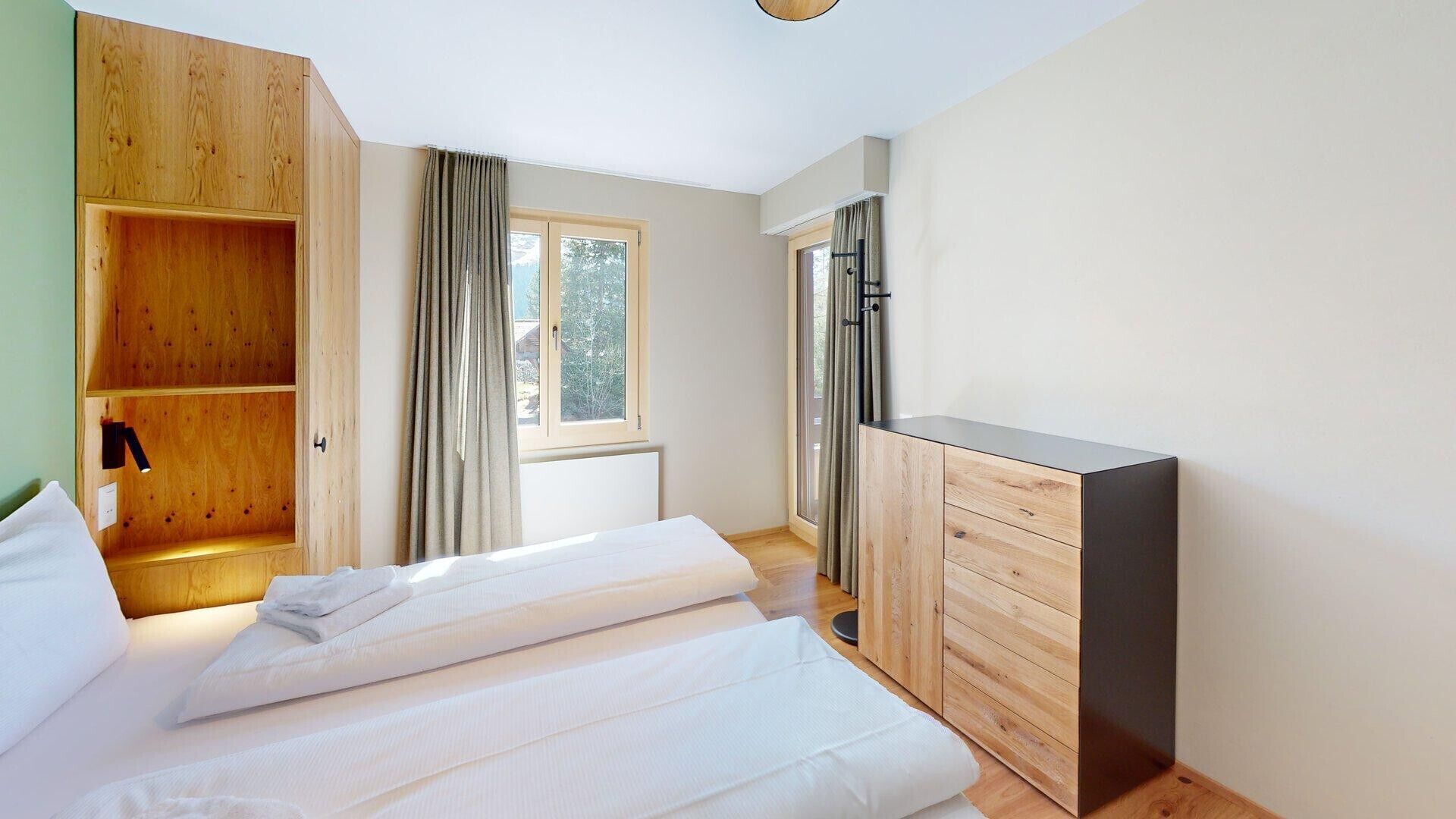 A bedroom with a bed, wooden wardrobe, and a window with curtains.