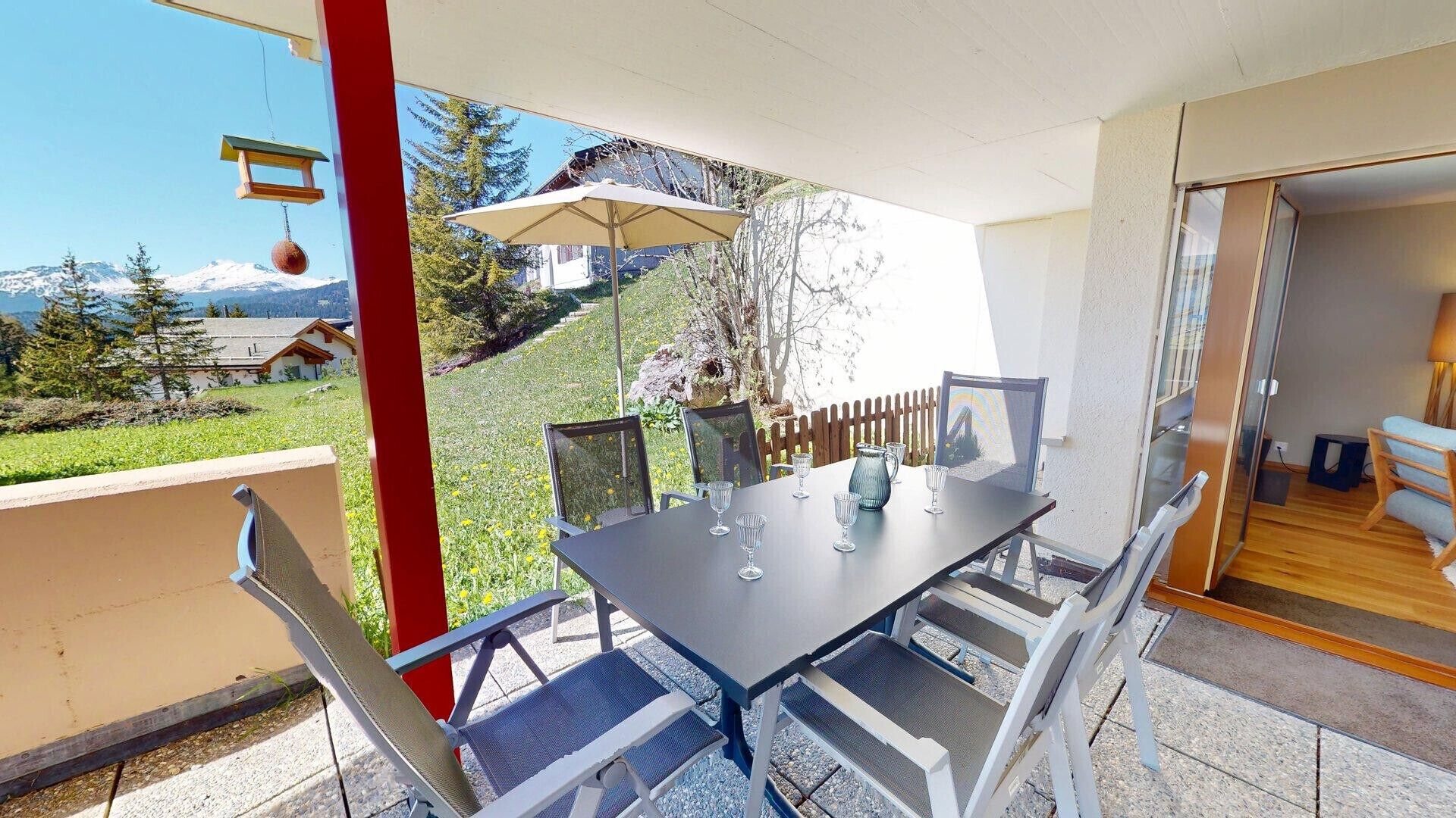 Ein Balkon mit Tisch und Stühlen, einer hängenden Lampe und Blick auf einen Berg sowie Bäume.
