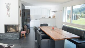 A modern kitchen with white cabinets, a stone accent wall, and a large window overlooking a green landscape. - Ski in-Ski out holiday flat Heimberg in Parpan- Lenzerheide (Parpan)