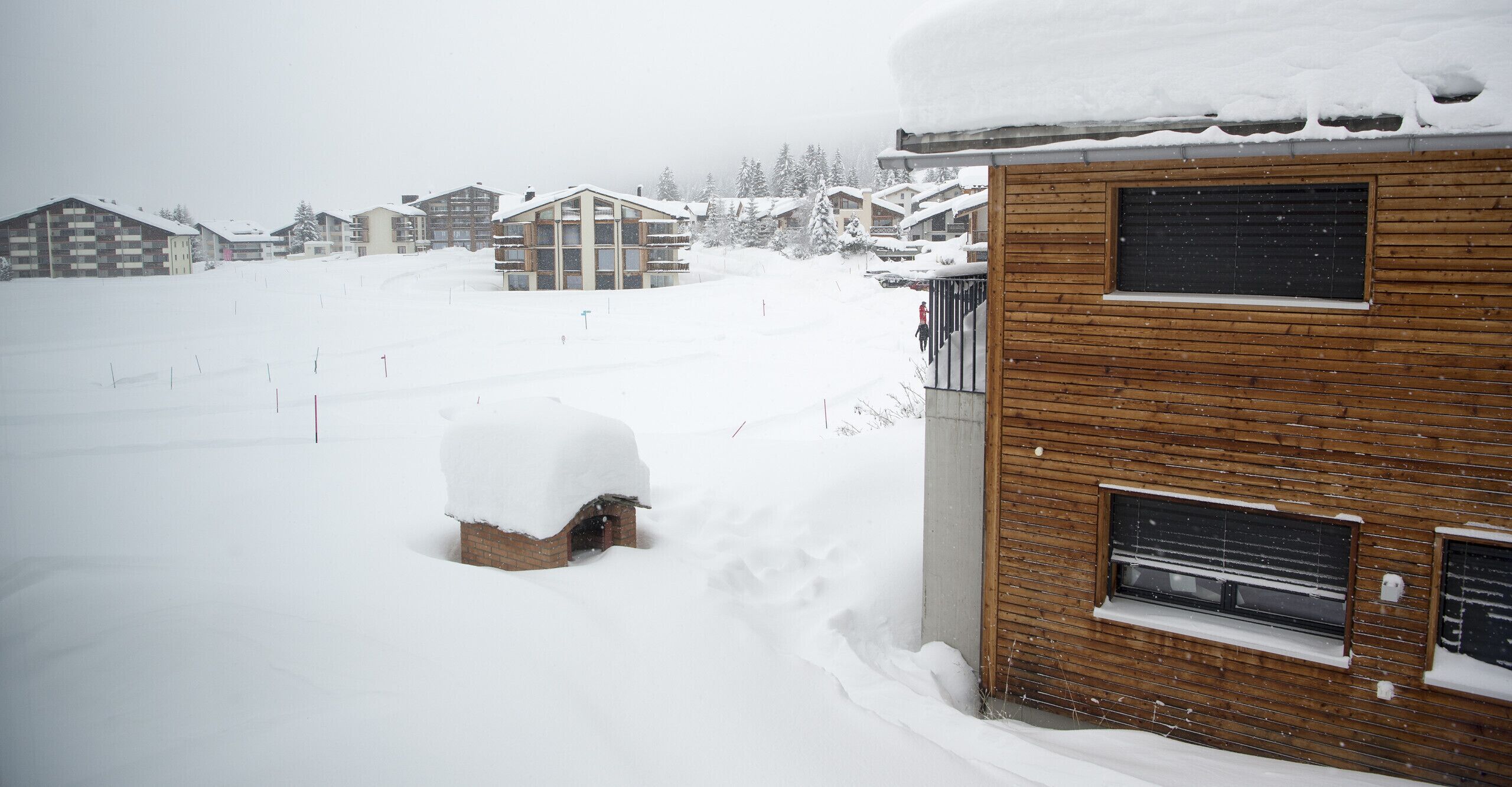 Una zona residencial cubierta de nieve con casas de madera y un edificio moderno con grandes ventanales.