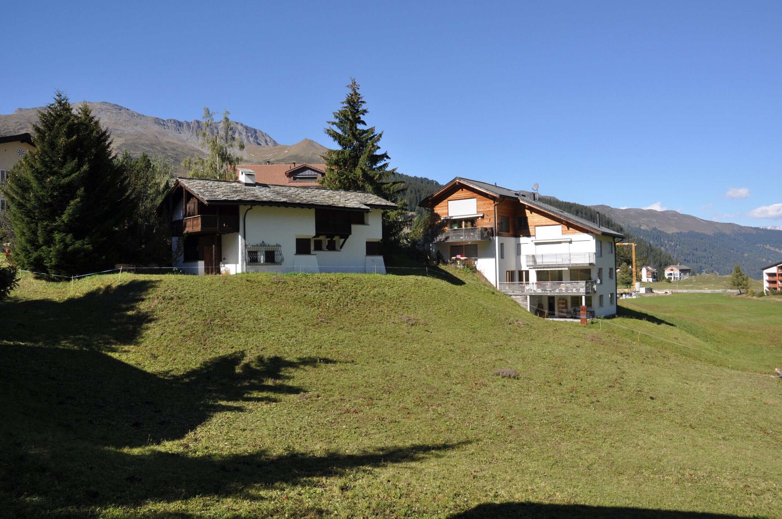 A hillside property with two main buildings, one with a balcony and another with a large window.