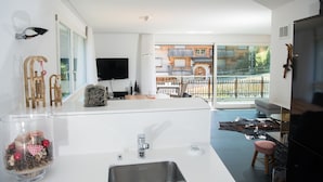 A modern kitchen with a large island, a flat-screen TV, and a view of a balcony with a wooden fence. - Ski in-Ski out holiday flat Heimberg in Parpan- Lenzerheide (Parpan)