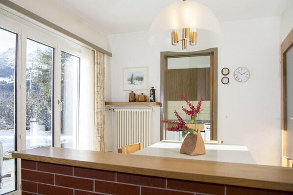 A modern kitchen with a wooden countertop, a dining table with chairs, a radiator, and a window with a view of snow-covered trees. - House with mountain views & a sun terrace (Valbella)