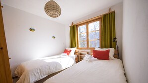 A room with two beds, a window with curtains, a hanging light fixture, and a small wall decoration.