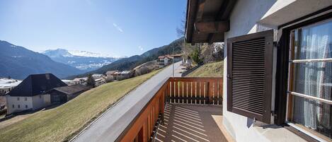 Un balcon offrant une vue sur des montagnes enneigées, un chemin pavé et une balustrade en bois.