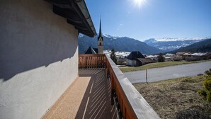 A balcony with a view of snow-capped mountains and a church steeple.