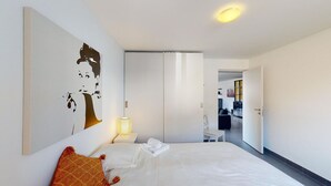 Una camera d'albergo con un letto, un comodino, una lampada, un quadro e un armadio.