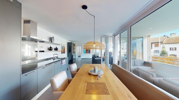 Una cucina moderna con un tavolo da pranzo in legno, un lampadario a sospensione e ampie finestre che offrono vista sull'esterno.