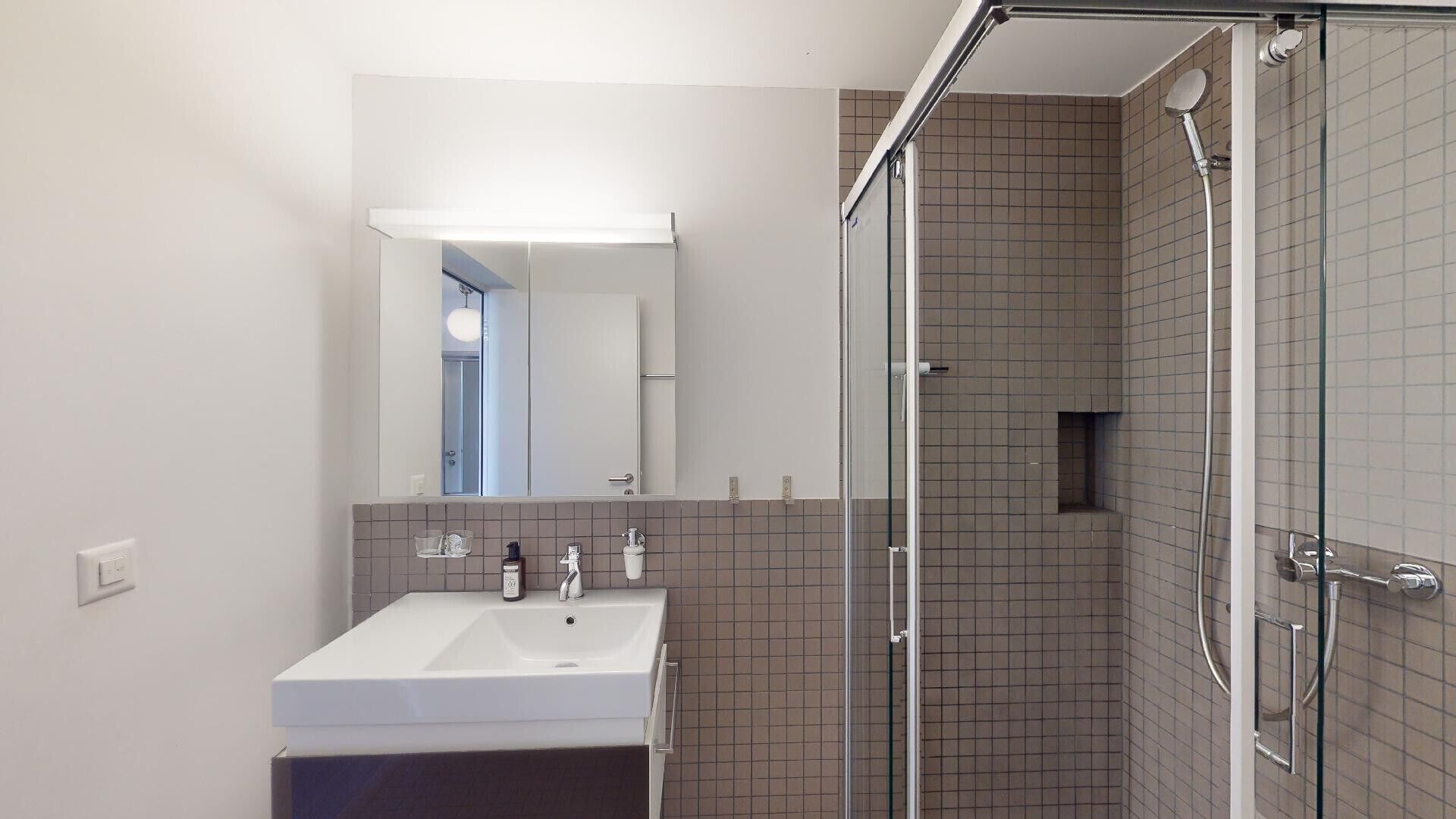 Un baño moderno con un lavabo, espejo y ducha blancos.