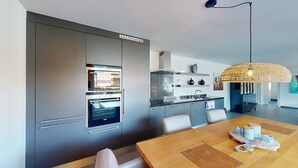 Una cucina moderna con elettrodomestici integrati, un'area pranzo con tavolo in legno e un lampadario intrecciato originale.