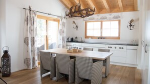 Una cocina moderna con techo de madera, una gran mesa de comedor con sillas a cuadros y una araña.