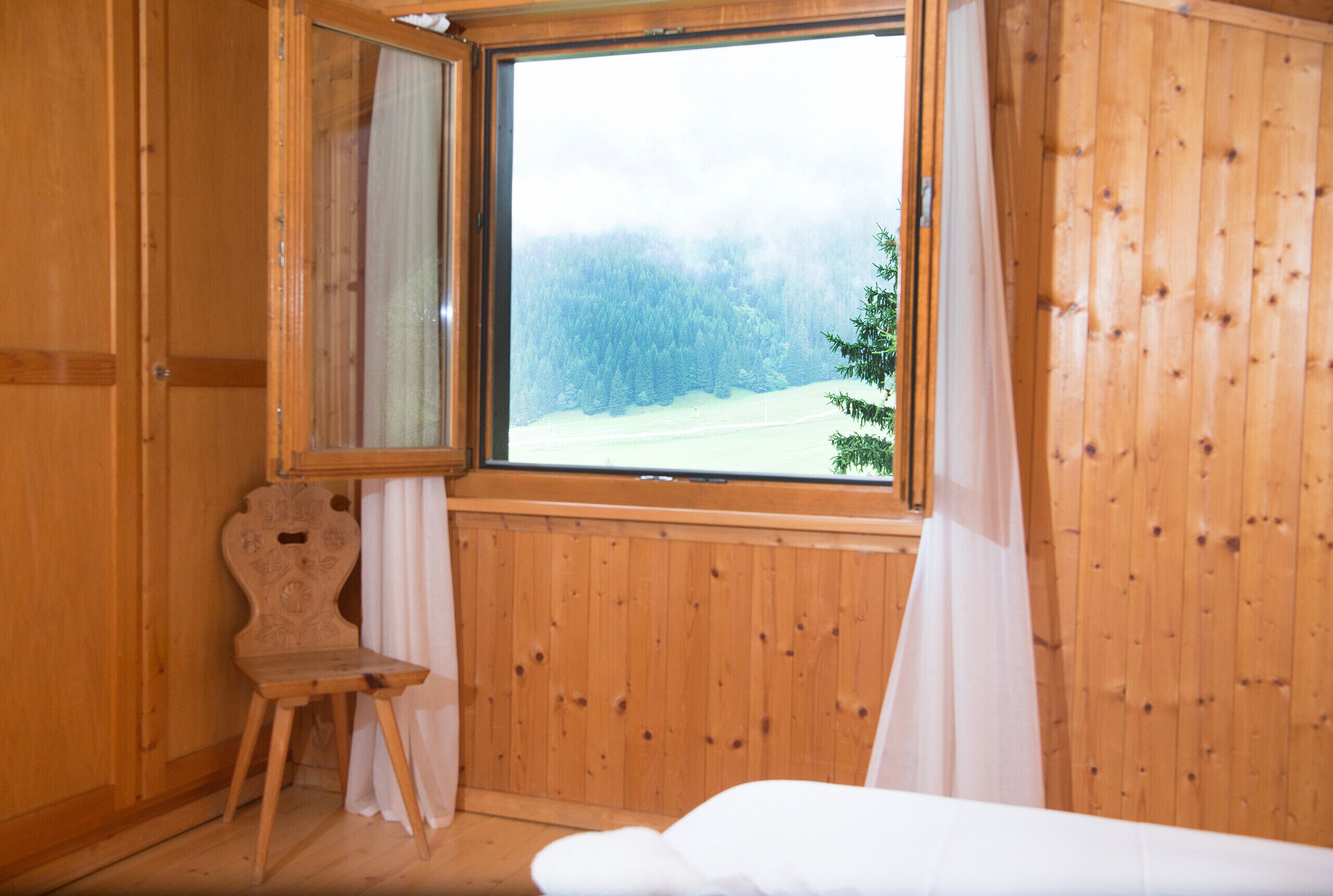 A wooden cabin room with a large window, a wooden chair, and a bed.