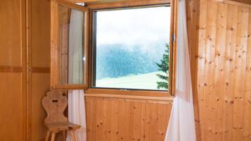 A wooden cabin room with a large window, a wooden chair, and a bed.