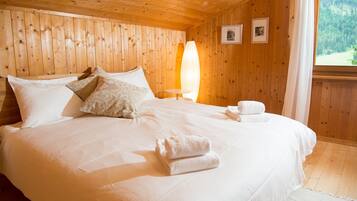 Een kamer met houten lambrisering, een bed, nachtkastje en raam met uitzicht op een bos.