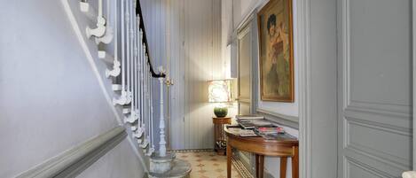 Un pasillo con una escalera, una mesa con revistas y un cuadro en la pared.