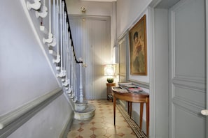 A hallway with a staircase, a table with magazines, and a painting on the wall.