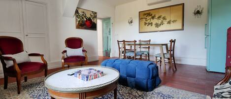 Una sala con una mesa redonda, dos sillones, un sofá, una mesa de comedor con sillas y un refrigerador.