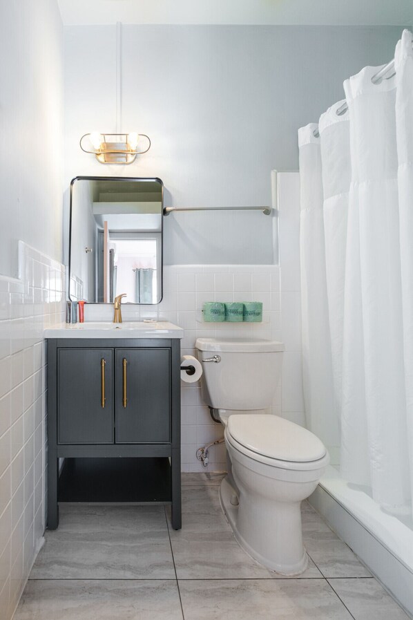 A bathroom with a toilet, sink, cabinet, mirror, and shower curtain.