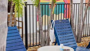 Outdoor seating with blue loungers, a small round table, and a colorful mural in the background.