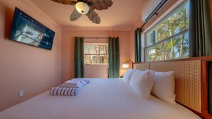 A hotel room with a bed, a ceiling fan, a TV mounted on the wall, and a window with curtains.