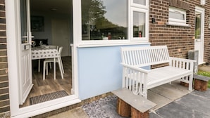 Una casa con un patio che include una panchina bianca, un tavolo con sedie e una finestra vista giardino.