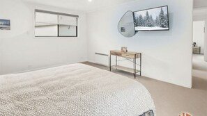 Ett modernt sovrum med en stor säng, ett sängbord, en spegel och en väggmonterad TV.