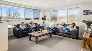 Ein Wohnzimmer mit vier Sofas, die um einen Couchtisch angeordnet sind, großen Fenstern mit satinierten Scheiben und einer dreibeinigen Stehlampe.